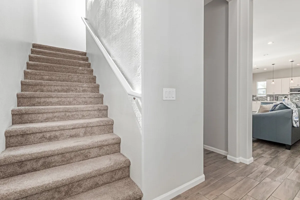 The image showcases the entryway and staircase of the home, with the living area visible in the background. The scene feels welcoming, representing the transition from outside to inside and the comfort awaiting after work.