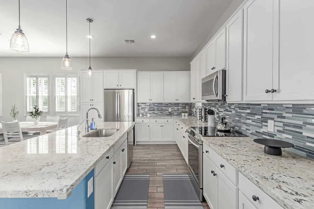 This interior shot displays a spacious, modern kitchen with granite countertops, stainless steel appliances, blue accent wall, and stylish pendant lighting. The space is bright and ideal for family meal preparation, gatherings, and entertaining after a day out.