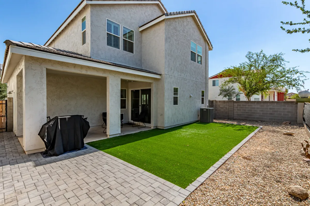 This image features a welcoming backyard space with artificial grass, a covered porch, and comfortable outdoor furniture. The scene is set for family gatherings, outdoor dining, relaxation, and enjoying the natural surroundings. The covered patio and well-maintained lawn suggest a perfect spot for post-adventure unwinding or family celebrations.