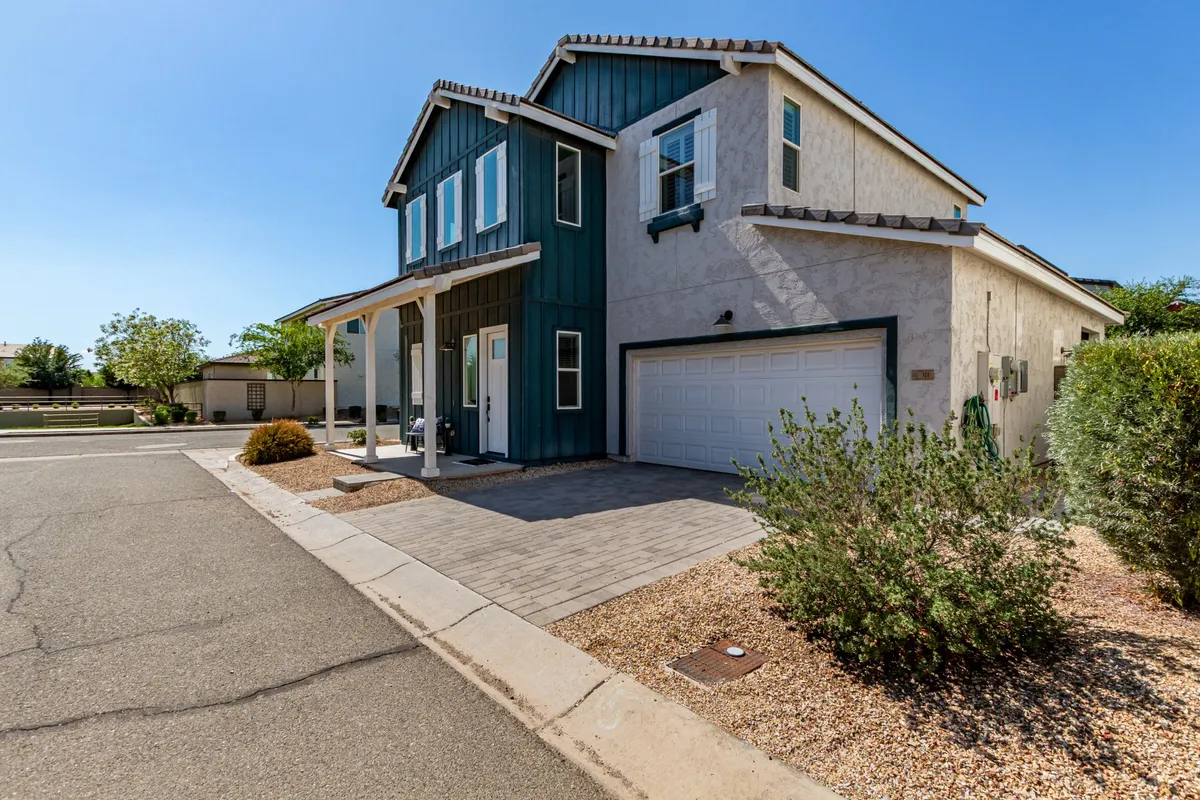 The home's attractive front porch with green siding, a garage door, and inviting pathway. The space is designed for outdoor relaxation, hosting friends, and taking in neighborhood energy, suggesting an easy transition from home base to area adventures.