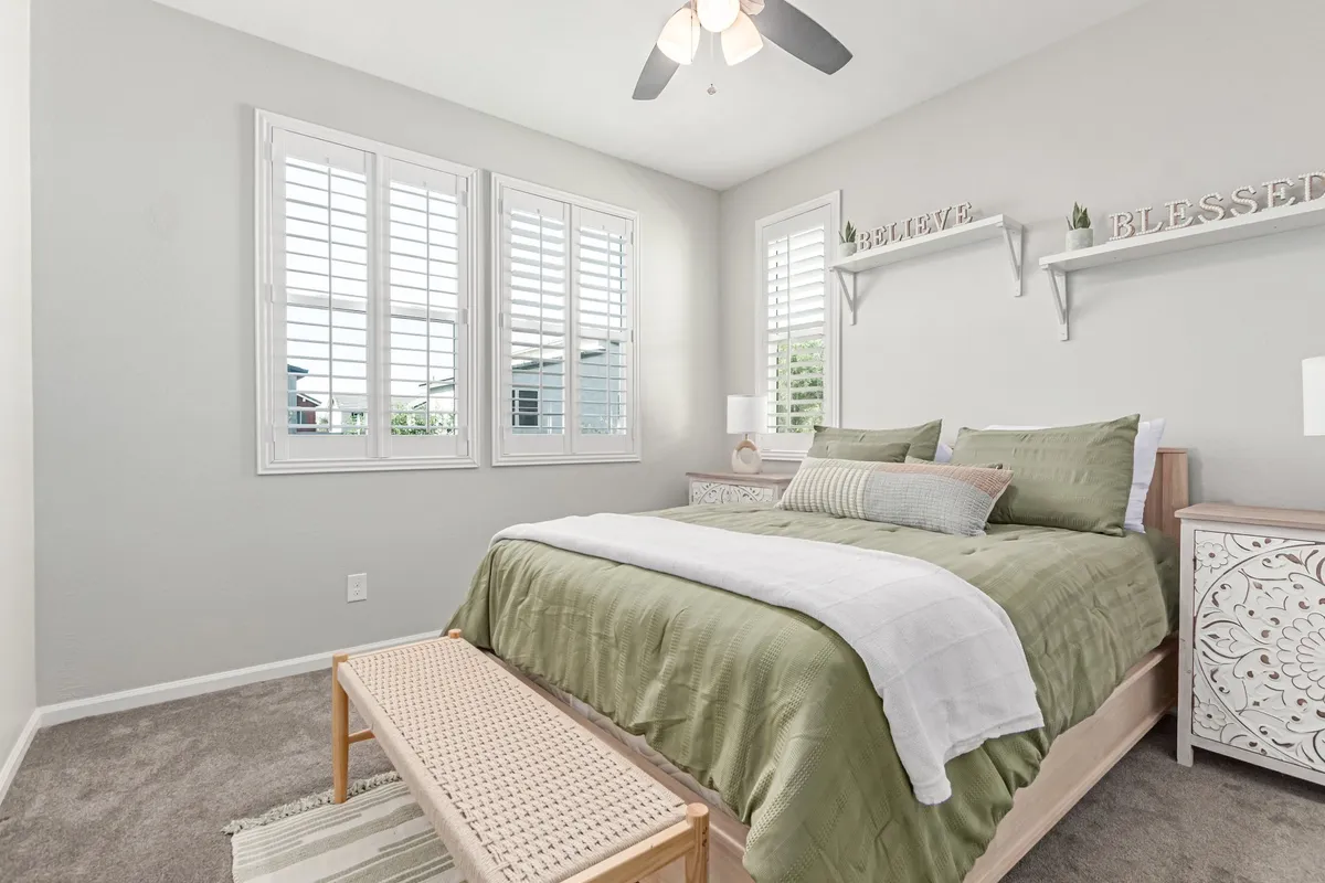 This image showcases a serene bedroom featuring a bed beside large windows that bathe the space in natural light. A decorative shelf and a cushioned bench offer both style and functionality, creating a space that’s ideal for relaxing or enjoying a quiet moment.