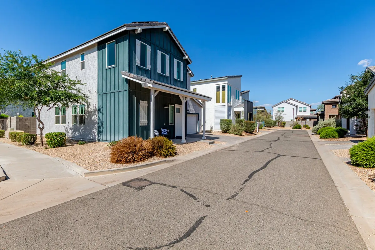 A charming exterior shot of a two-story house with blue siding, neat shrubs, and a paved road, capturing the tranquil atmosphere of a friendly, safe neighborhood.