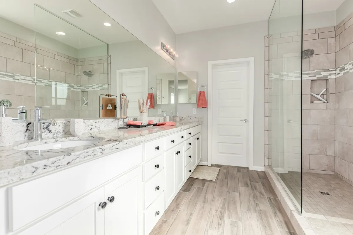 A modern, spa-like bathroom with a double vanity, expansive mirrors, and a glass shower enclosure. The clean lines and fresh ambiance evoke a sense of luxury and relaxation, perfectly suited for self-care routines or unwinding after a long day.