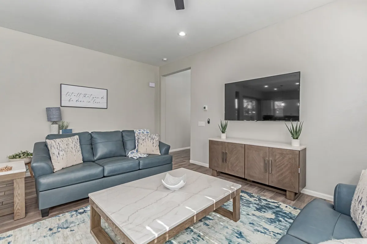 A spacious living room featuring a blue leather sofa, marble coffee table, large television, and modern decorative wall art. The room is arranged for comfort and group gatherings, ideal for relaxing together after a day out.