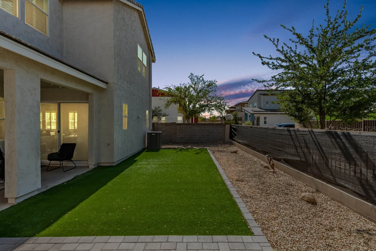 This image depicts the exterior of the home, featuring a lush green lawn, a paved pathway leading up to the house, large windows, and a calm atmosphere. The setting is bright and inviting, suggesting easy access and a peaceful place to return to after a busy day.