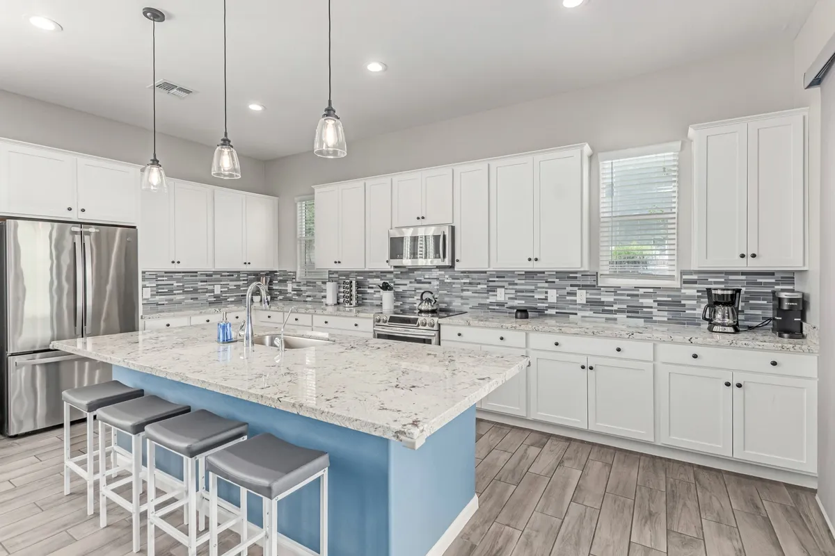 A kitchen scene centered on a large island, surrounded by modern appliances and a stylish tile backsplash. The open layout suggests room for multiple people to cook or gather, fostering a sense of community and hospitality.