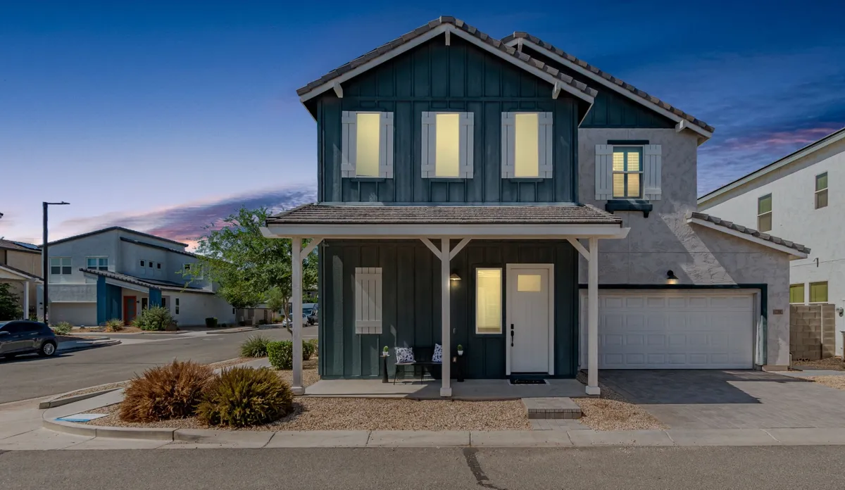 The image showcases the inviting exterior of a modern single-family home in Goodyear, Arizona. A welcoming front porch with comfortable seating sets the stage for relaxing evenings, while large windows hint at bright, airy interiors. Meticulously maintained landscaping and a spacious driveway with a garage complete the scene, creating an immediate sense of comfort and style.
