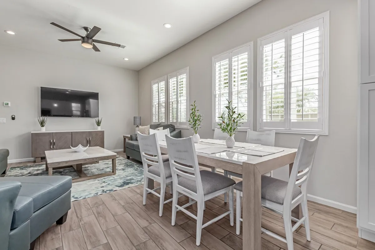 A welcoming living-dining combo featuring a comfortable sofa, a television for movie nights, a large window letting in sunlight, and a decorative touch with plants and artwork. The dining table is centrally located, ideal for sharing meals and conversations.