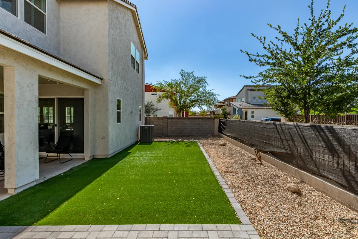 A peaceful backyard scene featuring a lush green lawn, a pebbled area, and the side of the house—ideal for outdoor gatherings or relaxing in the sun. The setting is informal and social, suggesting a space for friends to gather and unwind together after a day of exploring.