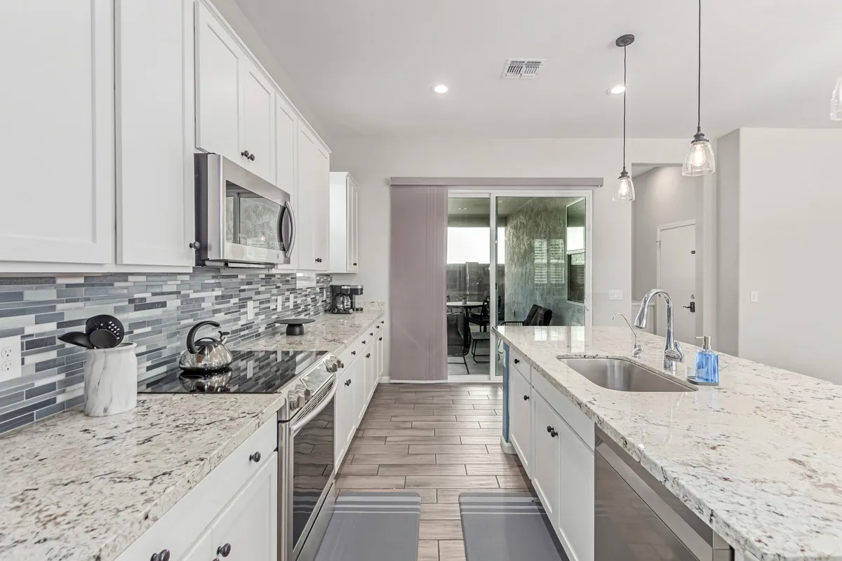 A modern kitchen environment featuring granite countertops, state-of-the-art appliances, a tile backsplash, and a central kitchen island. The setting exudes warmth and practicality, ideal for daily cooking and larger gatherings alike.